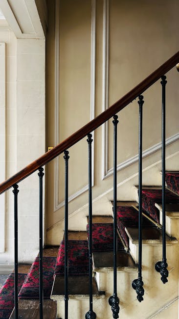 A view of an ornate Victorian staircase inside a historic property, featuring green-painted wooden stairs with decorative black and gold wrought iron balustrades and a polished wooden handrail. The st